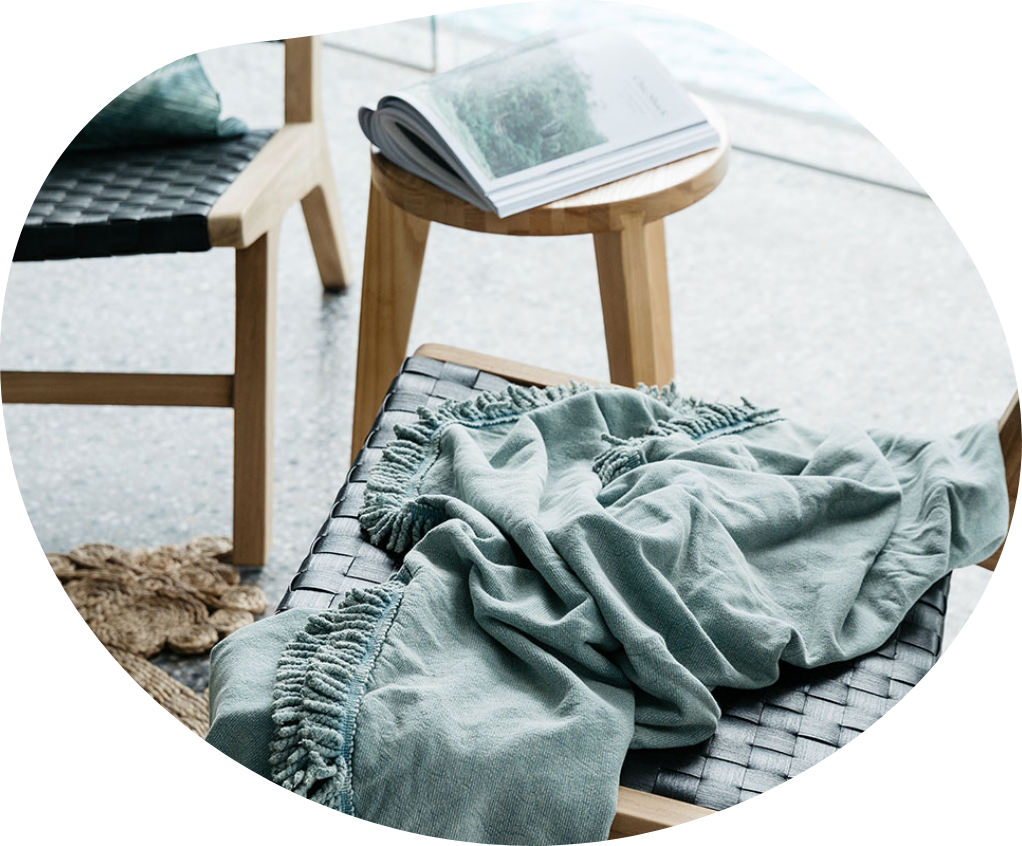 A sage green throw rug is draped over a timber chair with a wide thatch woven seat.